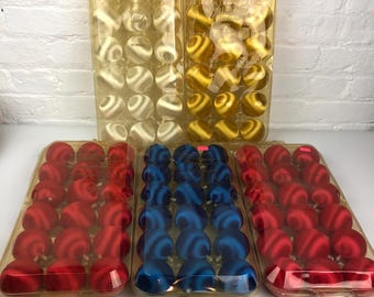 May include: Five clear plastic trays containing spherical ornaments in white, gold, blue, and red. Each tray holds twenty-four round ornaments with a satin-like finish. The trays are arranged in two rows, with the top row featuring white and gold.