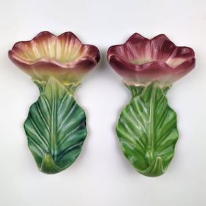 May include: A pair of ceramic wall pockets shaped like flowers with green leaves and petals that transition from yellow to deep magenta. Each piece features a sculpted leaf base and a wide, open blossom top with a glossy finish.