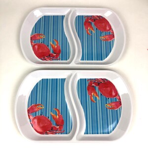 May include: Two white melamine divided serving trays, each featuring a blue and white vertical striped background with a vibrant red crab illustration. The trays have a smooth, glossy finish and a curved, organic shape with two distinct sections.