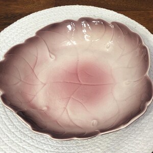 May include: A ceramic leaf-shaped dish with a glossy finish. The dish features a gradient of colors, transitioning from a deep mauve at the edges to a soft pink in the center. The leaf's veins are subtly raised, adding texture.