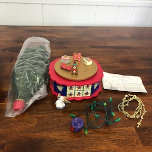 May include: A Christmas-themed decorative carousel with miniature presents, a teddy bear, and a red car. Also included are a small angel figurine, a string of green lights, a gold star garland, and a wrapped Christmas tree.