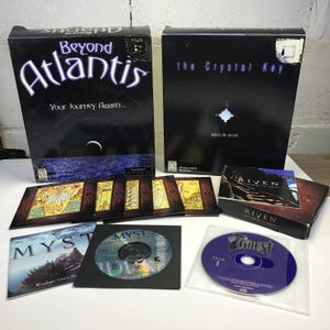 May include: A collection of PC game boxes and discs including Beyond Atlantis, The Crystal Key, Riven, and Myst. The set features various game cases, a Myst user manual, a Myst game disc, and a purple Zork Nemesis Disk 1 in a plastic sleeve.