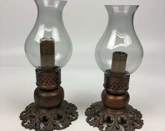 May include: Two antique-style glass candle holders with ornate bronze bases. The candle holders have a clear glass design and are perfect for adding a touch of vintage charm to any home decor.