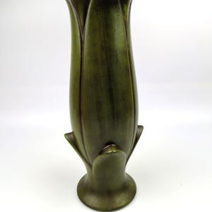 May include: A tall, olive green vase shaped like a closed tulip flower bud. The surface features a subtle, brushed texture with darker shading in the crevices between the petals. It has a flared circular base and a pointed, petal-like rim.