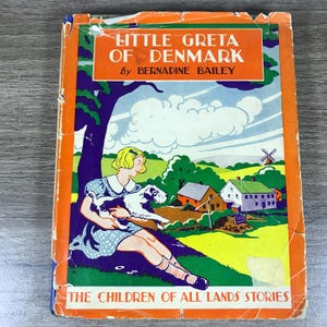 May include: A vintage hardcover book titled Little Greta of Denmark by Bernadine Bailey. The cover features a colorful illustration of a person with blonde hair sitting under a tree holding a black and white dog, with houses and a windmill.