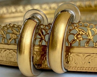 May include: A pair of gold hoop earrings with a brushed finish. The earrings have a silver band around the edge.