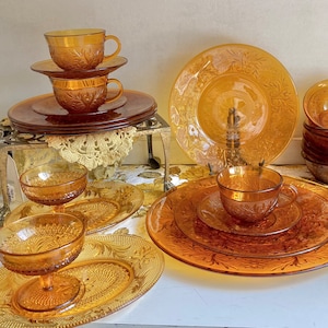 Può includere: Un set di piatti e tazze in vetro ambrato con un motivo floreale. Il set comprende un piatto grande, un piatto più piccolo, un piattino e due tazze. Tutti i piatti sono decorati con un delicato motivo floreale.