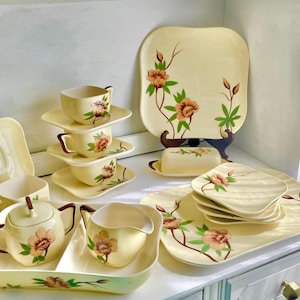 Puede incluir: Un juego de vajilla vintage con estampado floral en tonos crema, marrón y verde. El juego incluye una jarra, un azucarero, tazas de té, platillos y platos para servir.