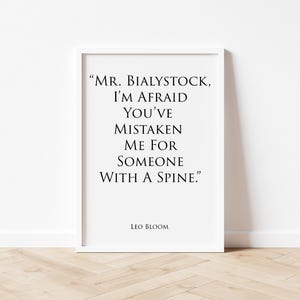 May include: A white framed wall art print featuring black text that reads: "MR. BIALYSTOCK, I'M AFRAID YOU'VE MISTAKEN ME FOR SOMEONE WITH A SPINE." The name "LEO BLOOM" is printed in smaller black text at the bottom of the white rectangular poster.