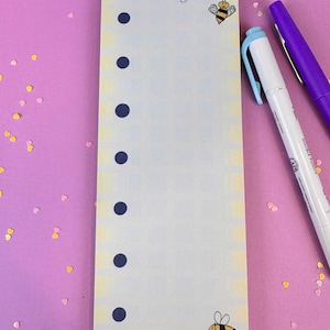 May include: A yellow notepad with a blue background and a bee illustration. The notepad has the text "Be A Busy Bee!" at the top and the text "Outfolded.org" at the bottom. The notepad has eight black dots down the left side.