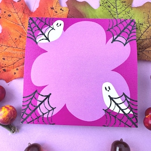 May include: A pink Halloween-themed card with a cloud-like shape in the center, featuring white ghost illustrations and black spiderwebs in the corners. The card is surrounded by fall leaves and decorative acorns.