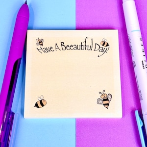 May include: A beige sticky note with the text "Have A Beautiful Day!" and four cartoon bees. The note is on a blue and purple background.