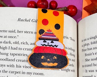 Könnte beinhalten: Orangefarbener und schwarzer Halloween-Lesezeichen mit einem mehrschichtigen Kürbisdesign. Der Kürbis hat ein schwarzes Gesicht mit einem breiten Lächeln und einen schwarzen Hut.