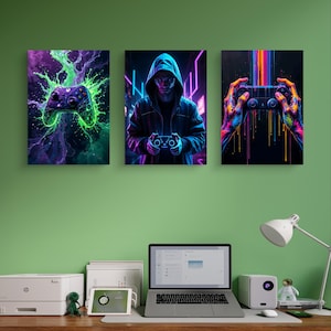 May include: Three framed gaming art prints. The first features a purple and green controller with a neon splash effect. The second shows a person in a hoodie holding a controller. The third shows hands holding a controller with colorful streaks.
