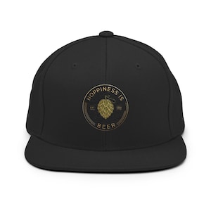May include: A black snapback cap featuring a circular embroidered patch on the front. The patch displays a gold-colored hop cone graphic in the center, surrounded by the text "HOPPINESS IS BEER" and "EST. 2020" in a circular arrangement.