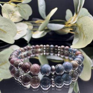 May include: A beaded bracelet featuring a mix of colorful gemstones. The bracelet showcases a variety of earth-toned beads, including shades of blue, brown, and pink. The beads are strung together with silver-colored spacers, creating a stylish accessory.