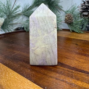 May include: A white and purple crystal point with a smooth, polished surface. The crystal is shaped like a pyramid and has a natural, organic look.