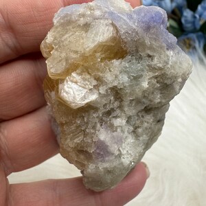 May include: A cluster of light brown and purple crystals with a rough, natural texture. The crystals are clustered together in a random, organic shape.