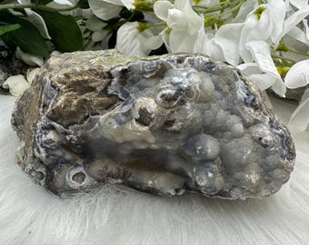 May include: A large, gray and brown agate geode with a rough, natural surface. The geode has a large, open cavity filled with smaller, white and gray crystals.