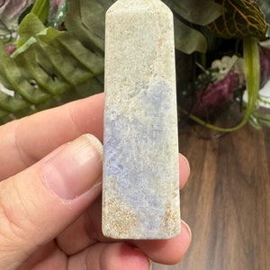 May include: A white and blue crystal point with a pointed top and a flat base. The crystal has a light blue and white swirl pattern.