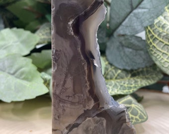 May include: A gray and white agate crystal point with a unique, natural pattern. The crystal is polished and has a smooth, glassy finish.