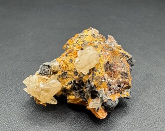 May include: A natural mineral specimen featuring a cluster of light-colored, crystalline formations on a matrix of brown, orange, and black rock. The crystals have a translucent appearance, contrasting with the earthy tones of the base material. The overall composition is rough and textured.
