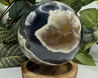 May include: A polished black and brown agate sphere on a wooden hexagonal stand. The sphere has a swirling pattern of black and brown agate.