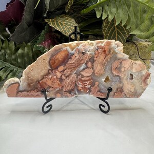 May include: A large, irregularly shaped slab of agate with a white, pink, and brown color scheme. The agate is on a black metal stand.
