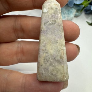 May include: A white and purple amethyst crystal point with a pointed top and a flat base. The crystal has a natural, rough texture and is translucent.