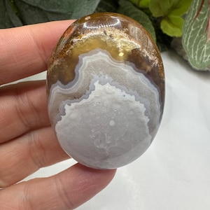 May include: A smooth, polished agate stone with brown, white, and gray banding. The stone has a natural, organic shape and is perfect for crystal healing or decoration.
