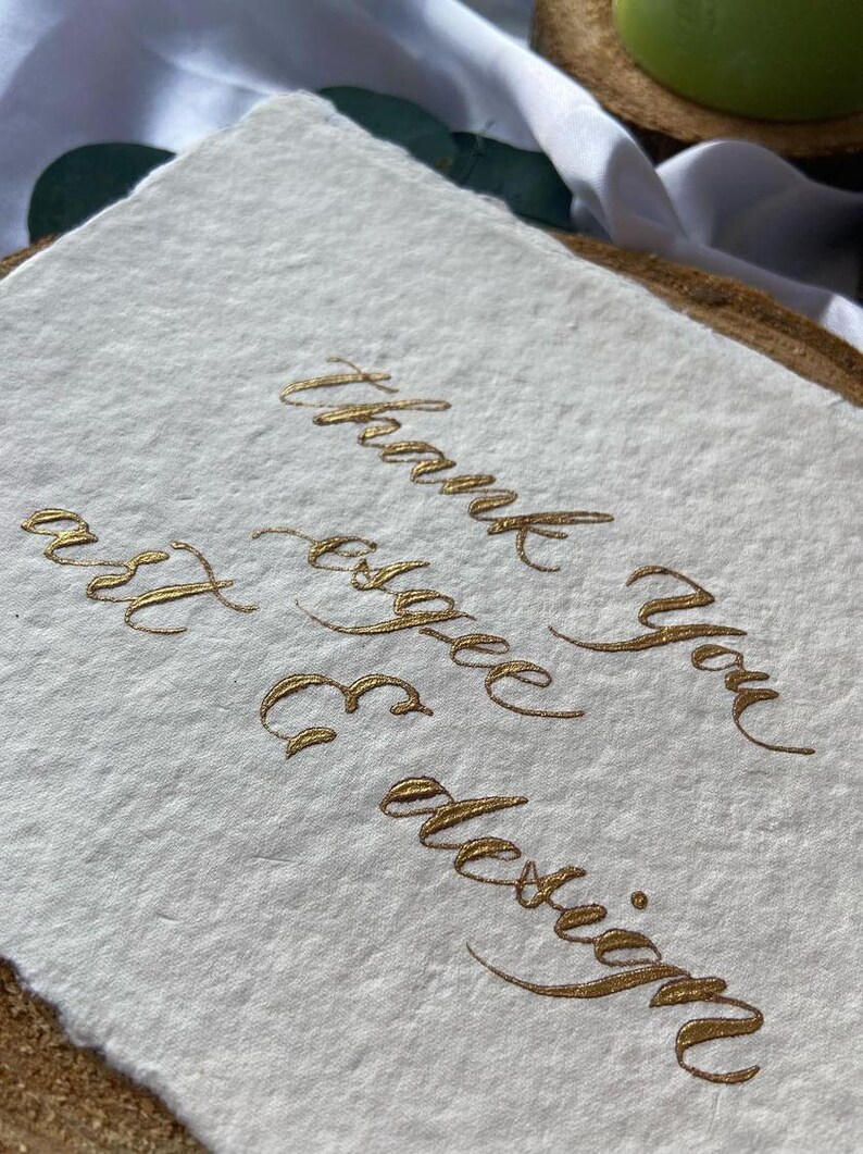 May include: A white card with the words "Thank you" and "for the design" written in gold calligraphy.