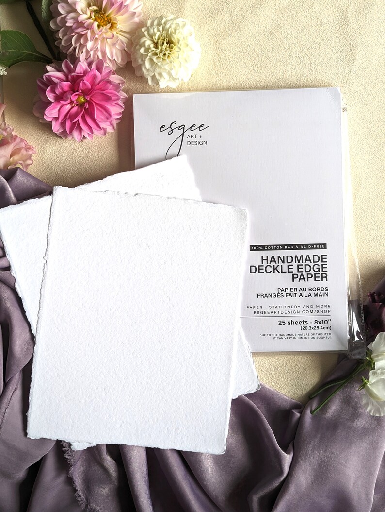 May include: A pack of 25 sheets of handmade, 100% cotton rag, acid-free, deckle edge paper. The paper is white and has a textured surface. The pack is labeled "Handmade Deckle Edge Paper" and includes the text "Papier au bords franges fait a la main".