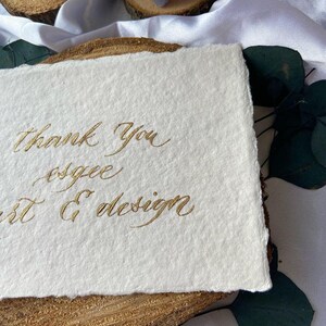 May include: A white card with gold calligraphy that reads "Thank you, esgee art & design".