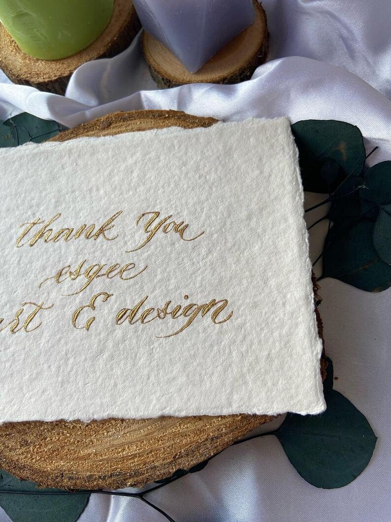 May include: A white card with gold calligraphy that reads "Thank you, esgee art & design".