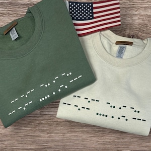May include: Two sweatshirts, one green and one cream, with the word "LOVE" written in braille on the front.