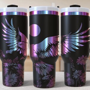 Op de afbeelding: Een zwarte reistumbler van roestvrij staal met een holografische afwerking. De tumbler heeft een ontwerp van een adelaar met zijn vleugels uitgespreid, omringd door bloemen. De tumbler heeft een handvat en een deksel.