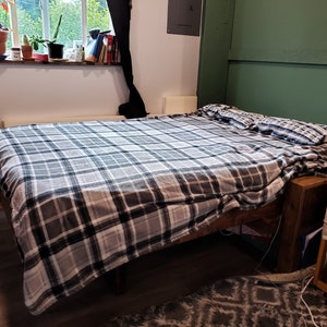 May include: A grey and white plaid bedspread on a wooden bed frame with a green wall behind it.