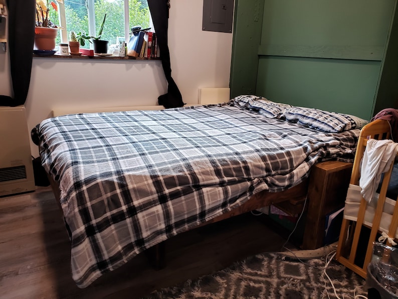 May include: A grey and white plaid bedspread on a wooden bed frame with a green wall behind it.