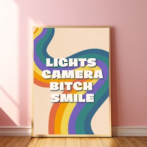 May include: A retro-style poster with a rainbow design and the text "LIGHTS CAMERA BITCH SMILE" in white letters.