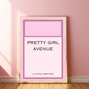Puede incluir: Un estampado rosa y dorado enmarcado con el texto "PRETTY GIRL AVENUE" y "A LITTLE FORTUNE". El estampado tiene un fondo rosa con un borde rosa y dorado. El estampado está apoyado contra una pared rosa.