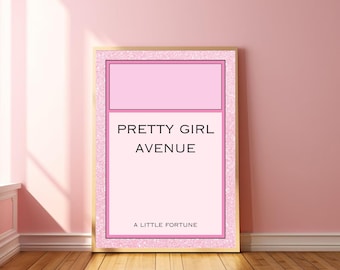 May include: A framed pink and gold print with the text "PRETTY GIRL AVENUE" and "A LITTLE FORTUNE". The print has a pink background with a pink and gold border. The print is leaning against a pink wall.