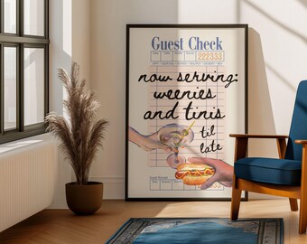 May include: A framed poster with the words "Guest Check" and "now serving: weenies and tinis til late." The artwork depicts a hand holding a martini and another holding a hot dog. A blue chair and a potted plant are in the background.