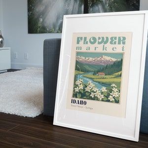 Może przedstawiać: Biały plakat w ramie z vintage'owym wzorem przedstawiającym g&oacute;rzysty krajobraz, rzekę i mały domek. Plakat głosi "Flower Market Idaho State Flower - Syringa".