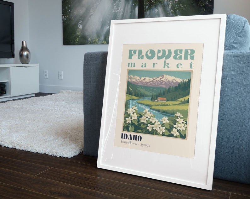 Może przedstawiać: Biały plakat w ramie z vintage'owym wzorem przedstawiającym g&oacute;rzysty krajobraz, rzekę i mały domek. Plakat głosi "Flower Market Idaho State Flower - Syringa".