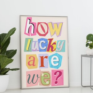 Op de afbeelding: Een kleurrijk ingelijst print met de tekst "how lucky are we?" in een stijl van uitknippen uit een tijdschrift.