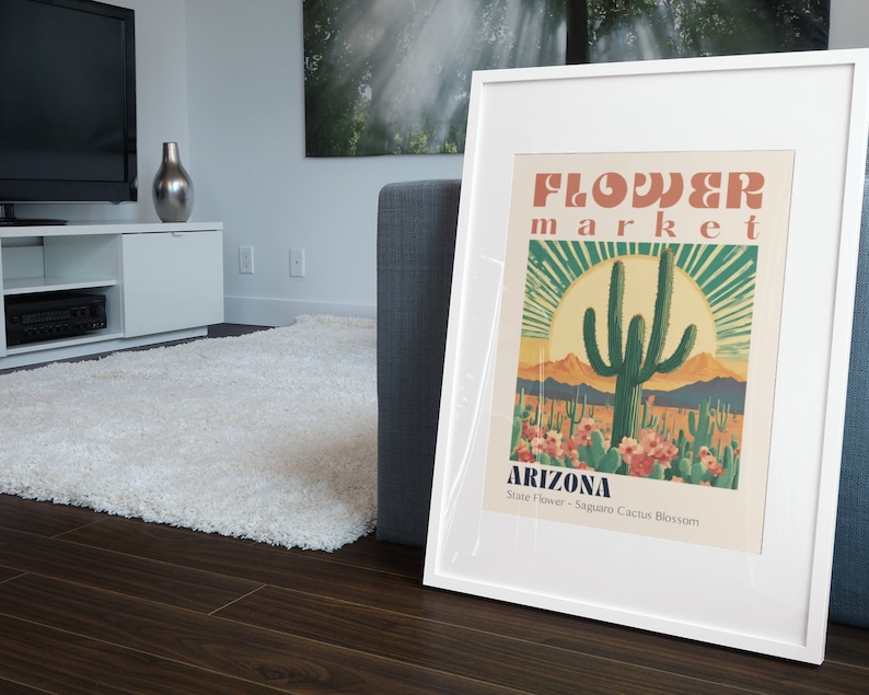 Op de afbeelding: Een wit ingelijste poster met een vintage ontwerp met een Saguaro-cactus in een woestijnlandschap. De poster luidt "Flower Market Arizona State Flower - Saguaro Cactus Blossom".