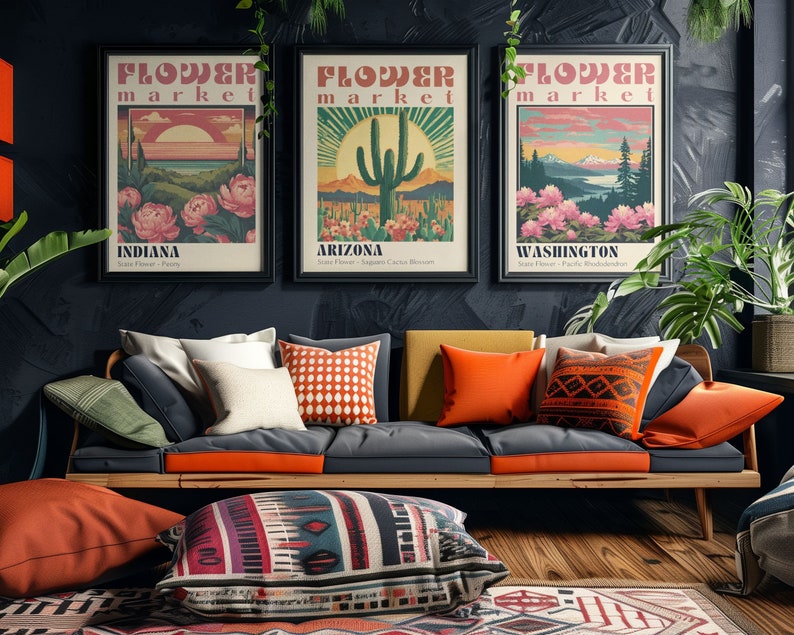 Może przedstawiać: Trzy plakaty w stylu vintage z tekstem "Flower Market" i nazwami r&oacute;żnych stan&oacute;w: Indiana, Arizona i Waszyngton. Plakaty przedstawiają ilustracje kwiat&oacute;w, kaktusa i g&oacute;rskiego krajobrazu. Plakaty wiszą na ciemnej ścianie nad sofą z pomarańczowymi i wzorzystymi poduszkami.