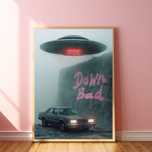 May include: A vintage brown car with a faded pink "Down Bad" graffiti on a cliff in the background. A flying saucer hovers above the car.