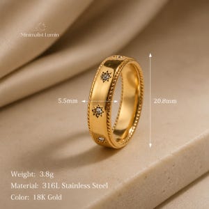 Peut inclure: Une bague dor&eacute;e orn&eacute;e de gravures en forme d'&eacute;toile avec des pierres incrust&eacute;es, bord&eacute;e d'une texture torsad&eacute;e. La bague mesure 5,5 mm de largeur et 20,8 mm de diam&egrave;tre. Elle est en acier inoxydable 316L, p&egrave;se 3,8 g et porte le nom Minimalist Lumin.