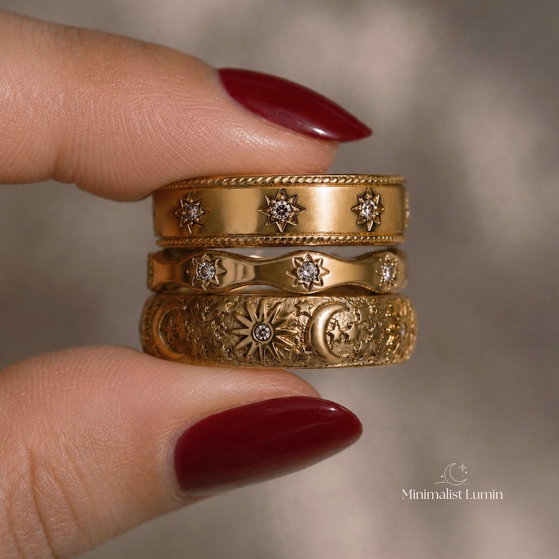 Peut inclure: Une pile de trois bagues dor&eacute;es. La bague sup&eacute;rieure pr&eacute;sente un bord textur&eacute; en corde et des motifs d'&eacute;toiles avec de petites pierres claires. La bague du milieu a un bord ondul&eacute; et des gravures d'&eacute;toiles. La bague inf&eacute;rieure affiche un motif.